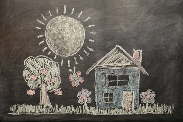 Drawing of a scenery including a house, a tree and sun on a blackboard with chalk.